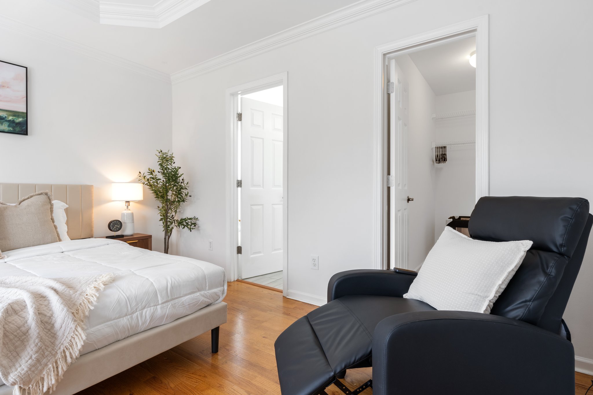Spacious master bedroom with queen bed, lounge chair, wooden nightstands, and sliding door to private balcony