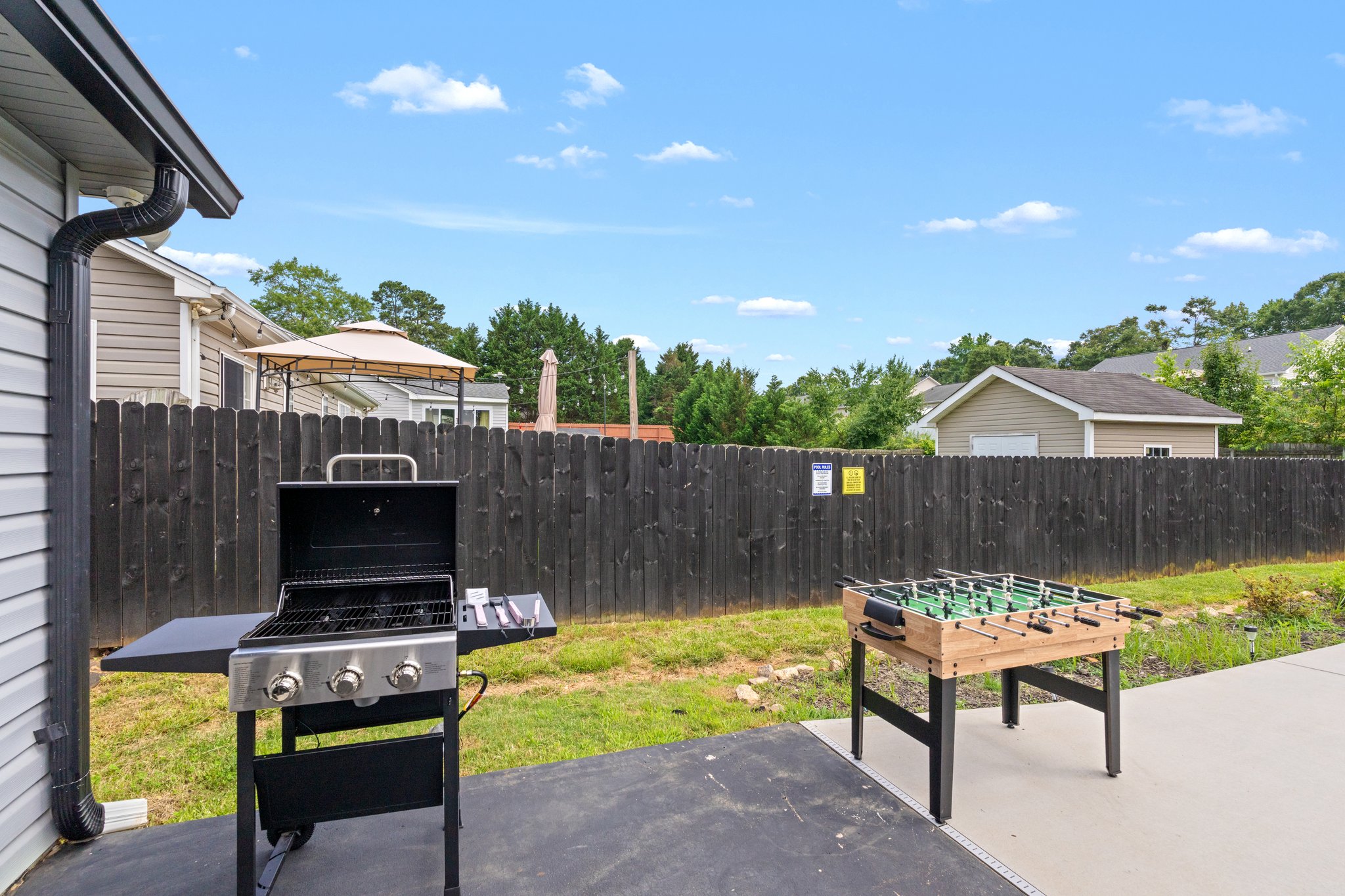 Spacious backyard entertainment area with professional gas grill, foosball table, and fenced patio in Greenville