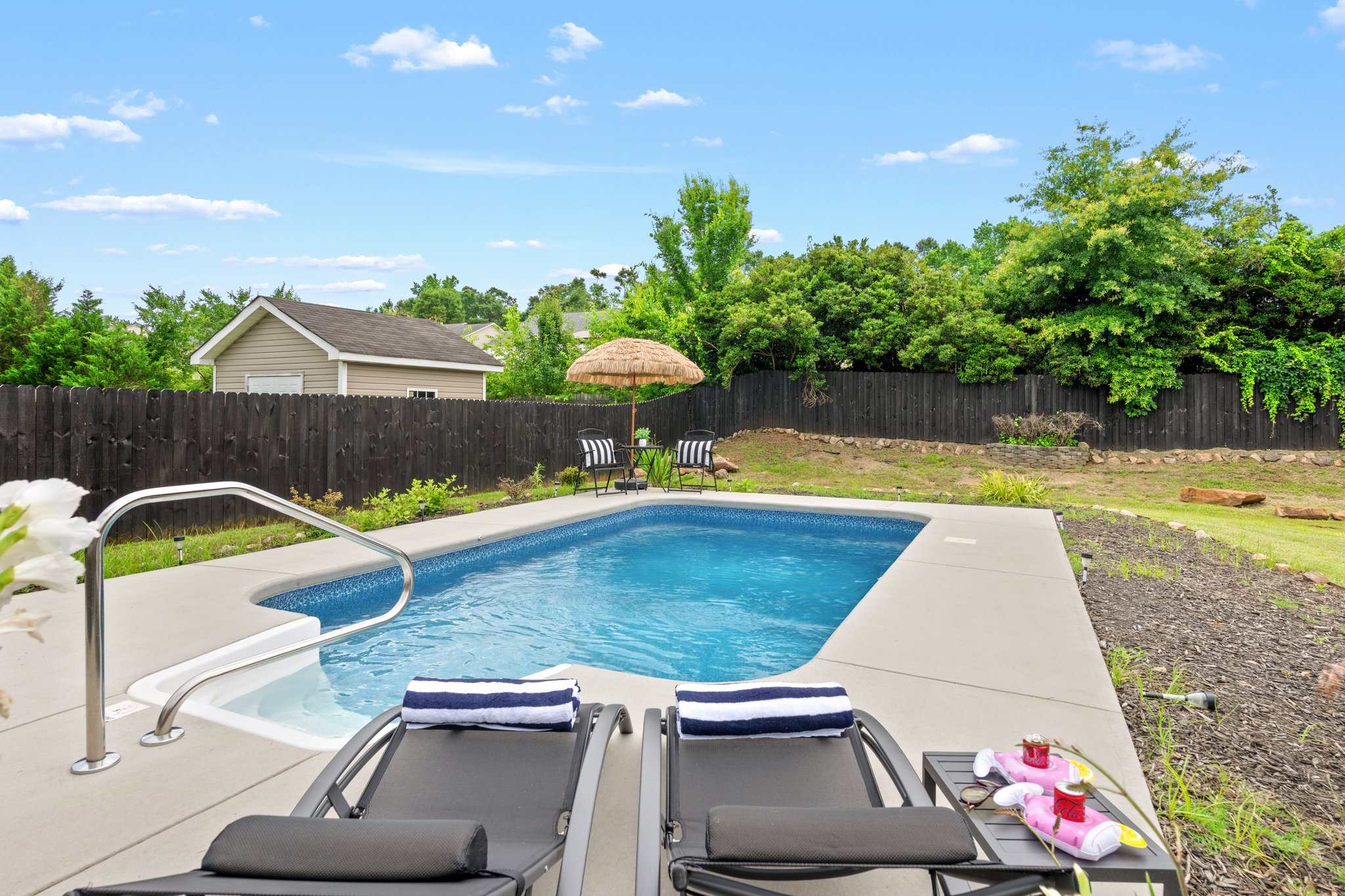 Resort-style private pool with lounge chairs, white concrete deck, and lush landscaping at Greenville home