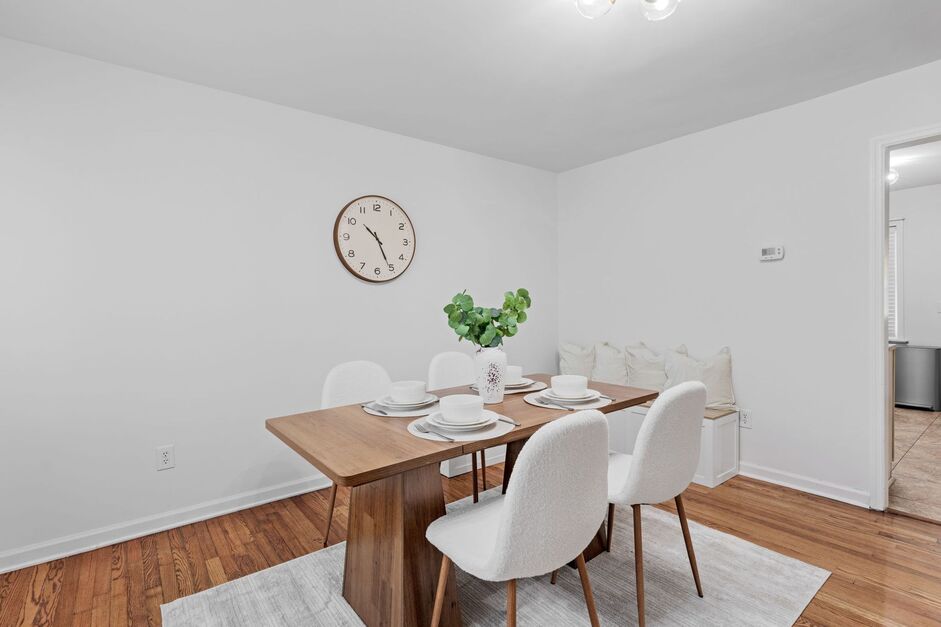 Bright dining area with wooden table, white chairs, wall clock, and access to living spaces at Clemson vacation home