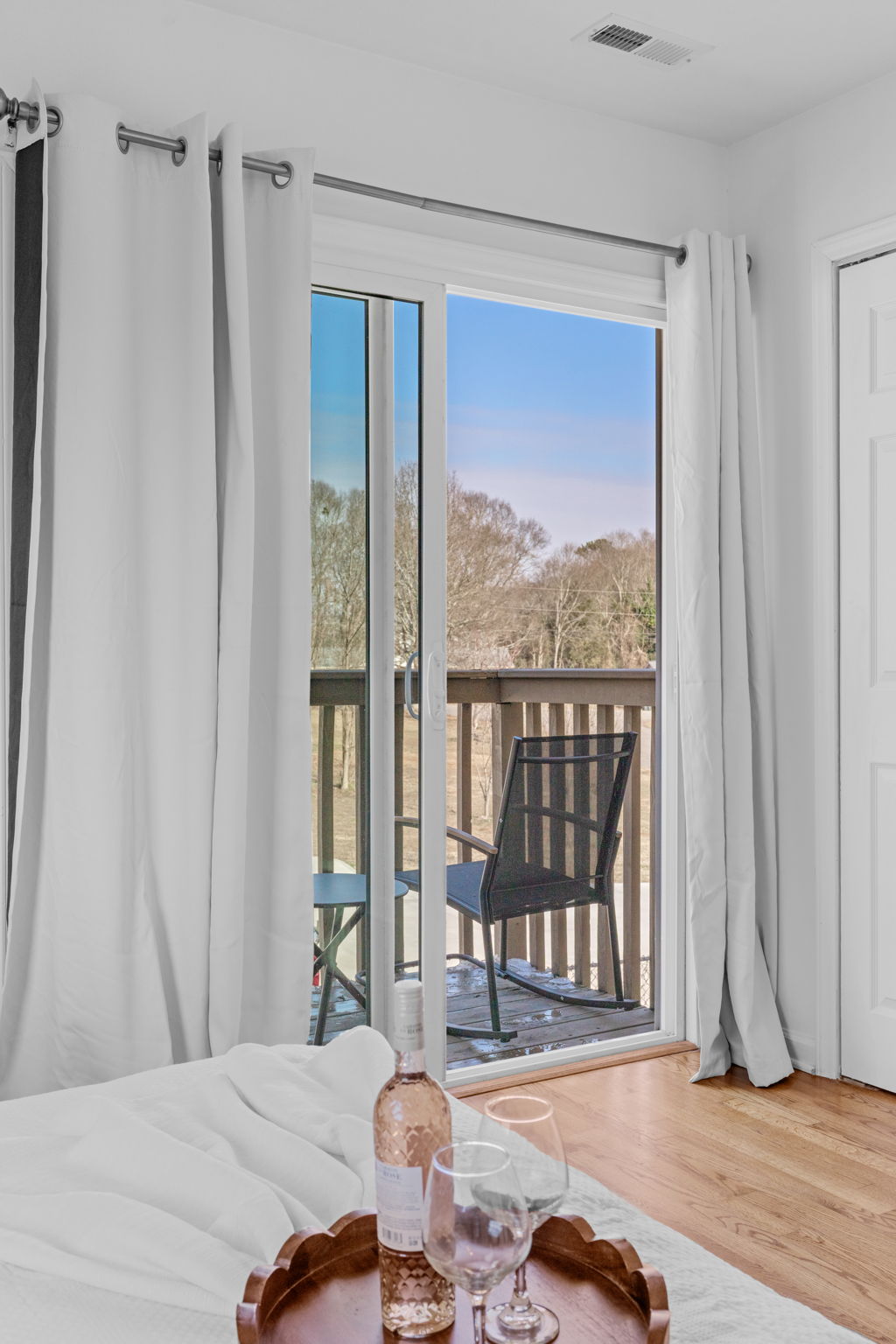 Master bedroom with white linens, French doors opening to private balcony with forest views near Clemson