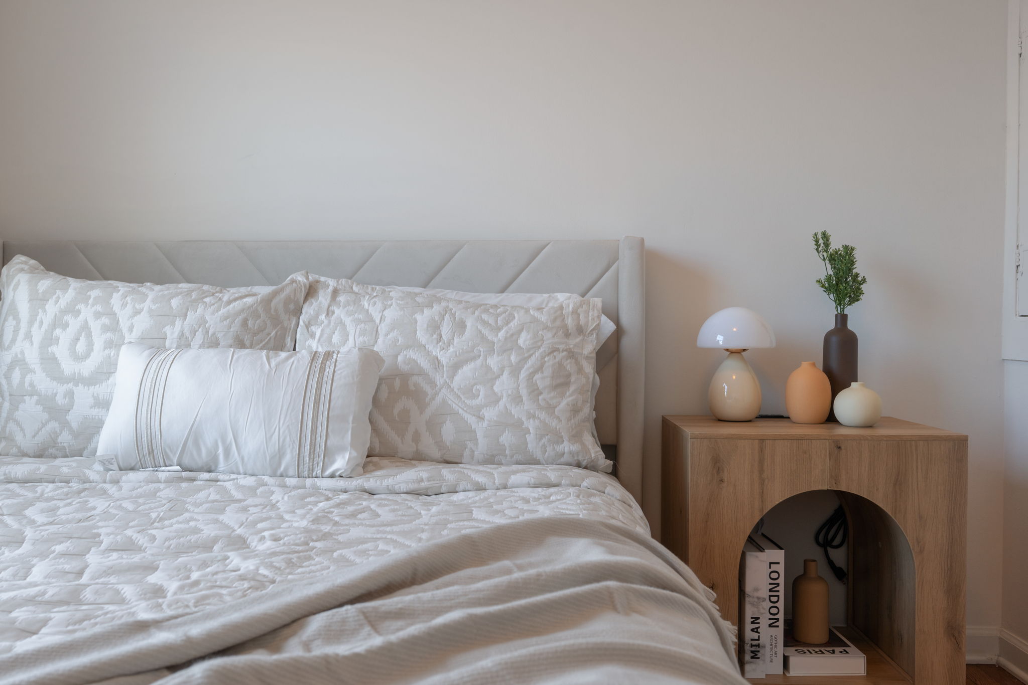 Serene master bedroom with white quilted headboard, layered pillows, and minimalist bedside with decorative objects