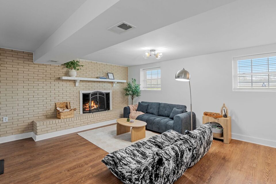 Open-concept living room with brick fireplace, dark sofa, wooden coffee table, and abundant natural light near Clemson