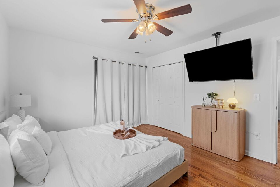 Luxurious master suite with queen bed, white linens, ceiling fan, dresser, and sliding glass door to private deck